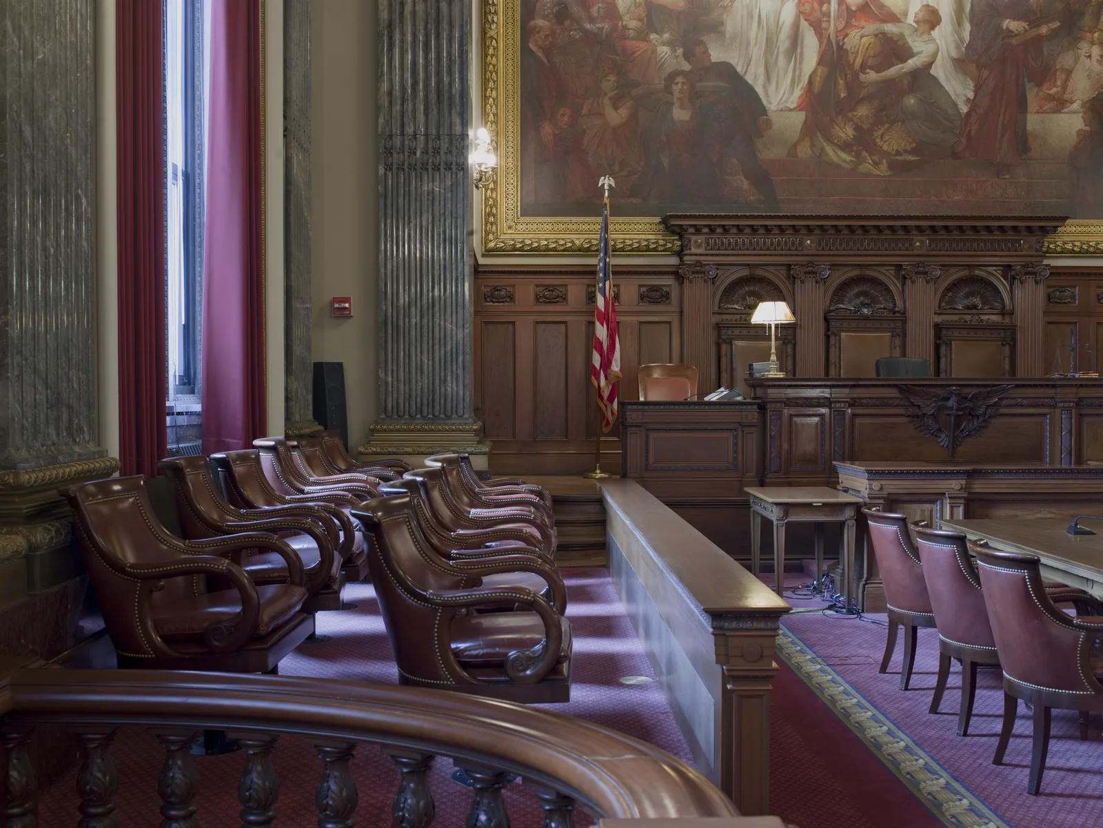 Wood-paneled federal courtroom with the judge's raised bench at center and an empty jury box of twelve seats to the right, lit by tall arched windows.