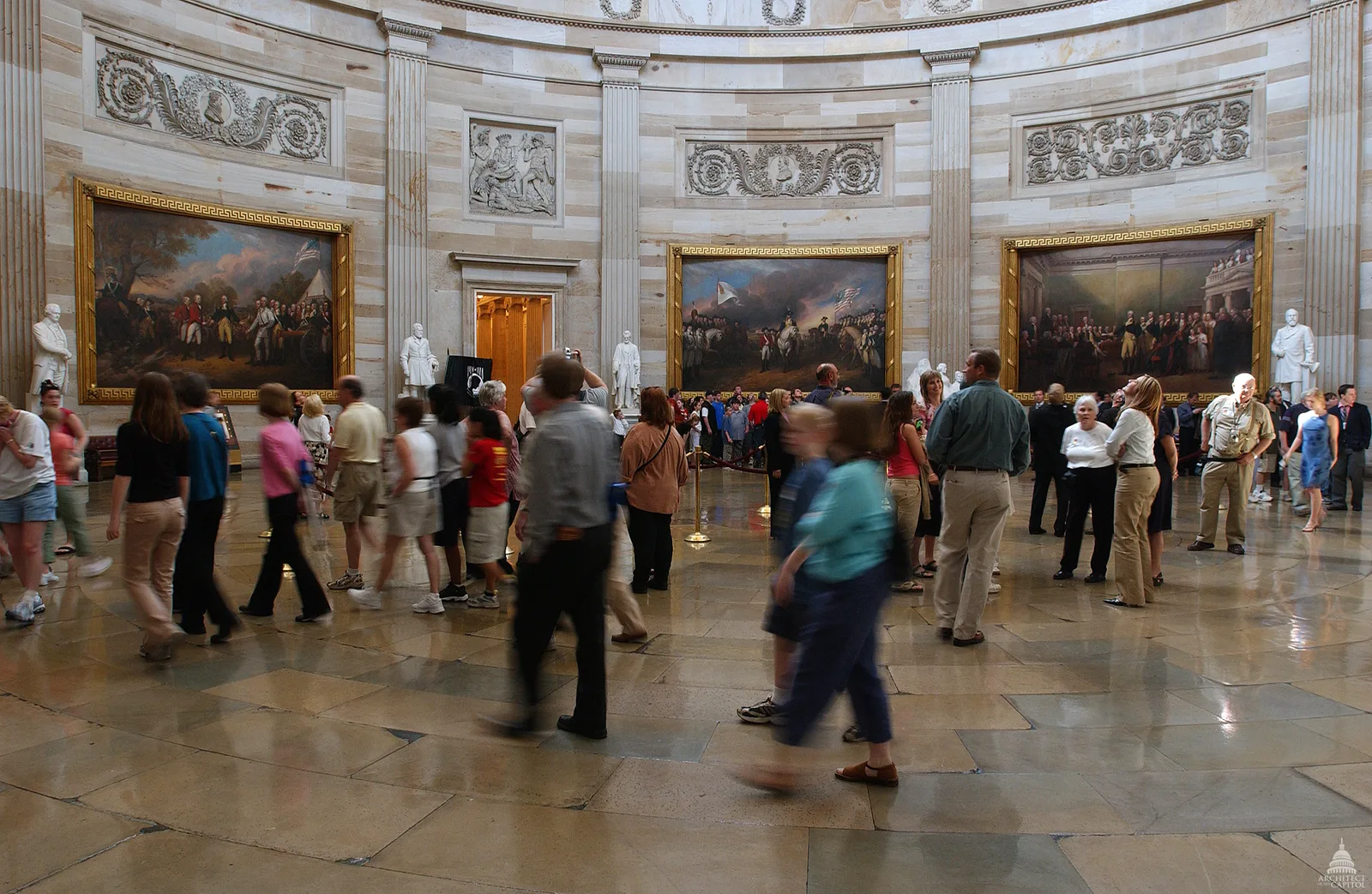 Interior of the U.S. Capitol Rotunda, with statues and historical paintings lining the curved marble walls