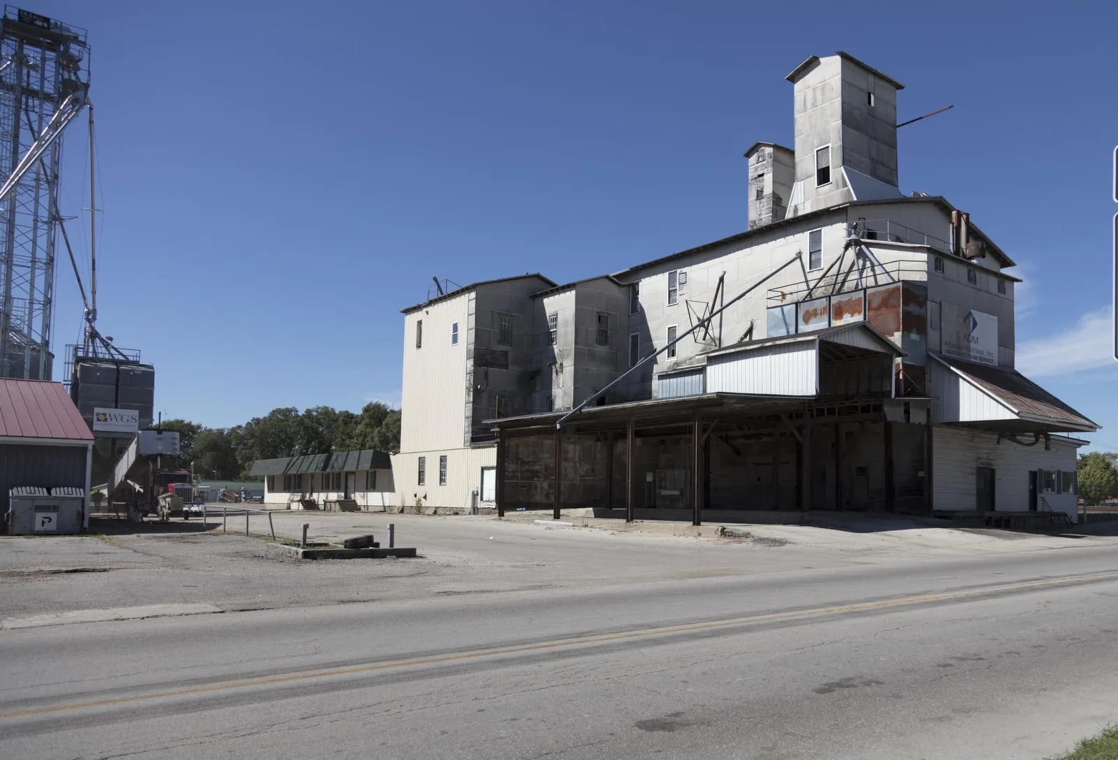 A grain elevator and farm service building along an empty road in small-town rural America