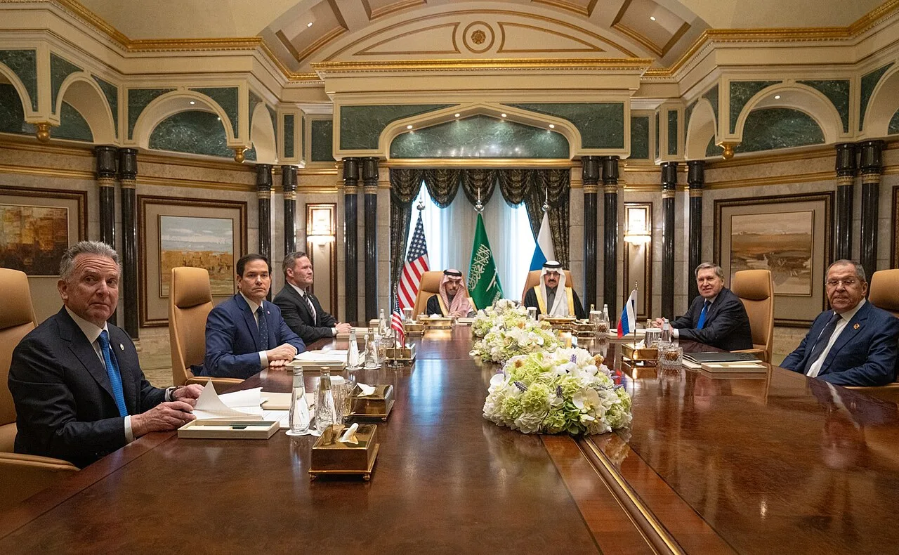 U.S. diplomats and foreign officials seated at a formal negotiating table during an official diplomatic meeting.