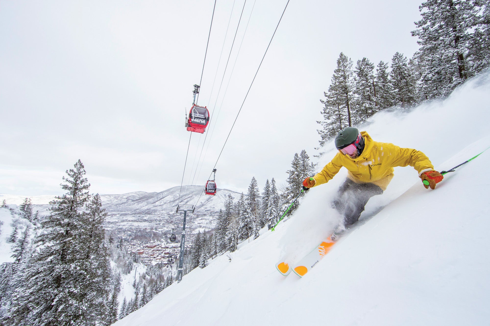 Skiers descending groomed slopes at a Colorado mountain resort with snow-covered peaks rising in the background